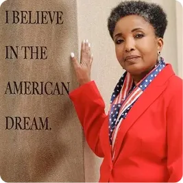 Dr. Carol Swain posing next to wall that says "I BELIEVE IN THE AMERICAN DREAM"