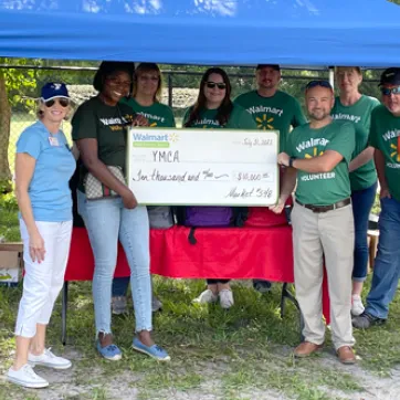 walmart volunteers and YMCA of the Suncoast leaders standing outside under blue tent, smiling and holding check presentation for $10,000 donation